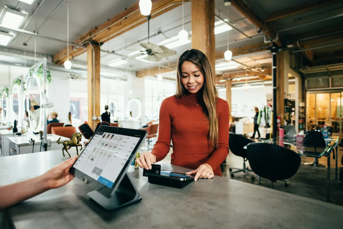 Illustrative stock photograph of a customer using a card terminal beside a point of sale screen.