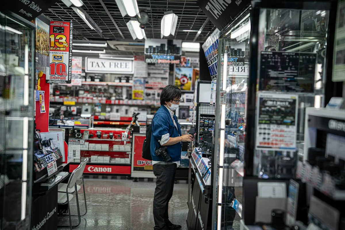 Illustrative stock photograph: A shopper inspecting cameras in an electronics retail store.