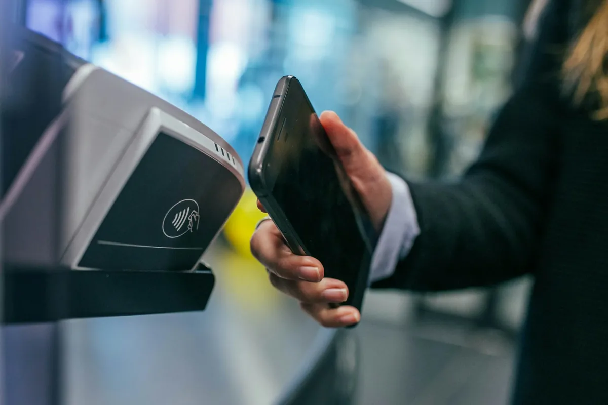 Illustrative stock photograph: Smartphone held near a contactless payment terminal.