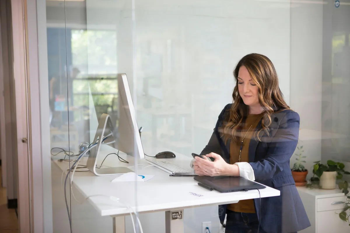 A professional checking her phone at a standing desk in a modern office
