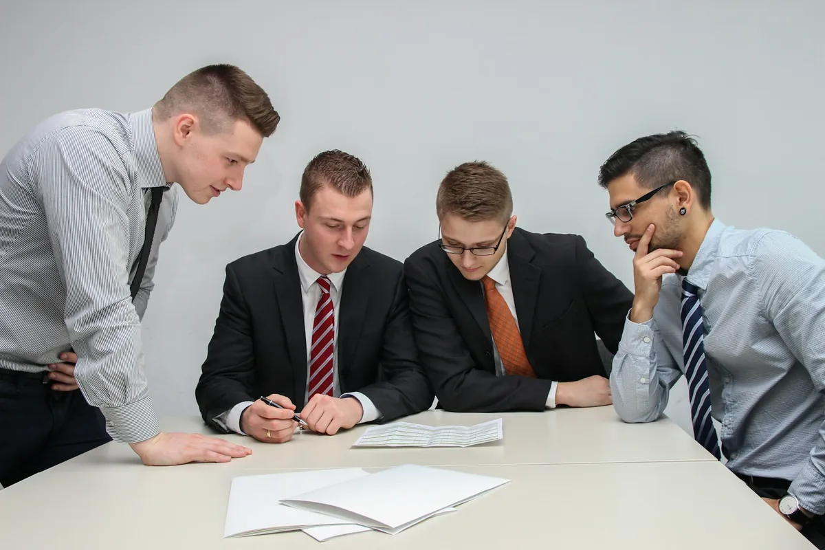 Four business professionals in shirts and suits review a printed document at a table.