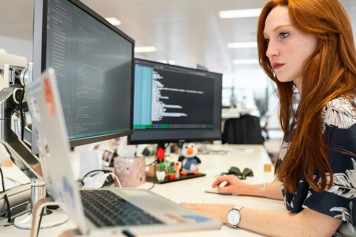Software engineer examining code on multiple computer screens