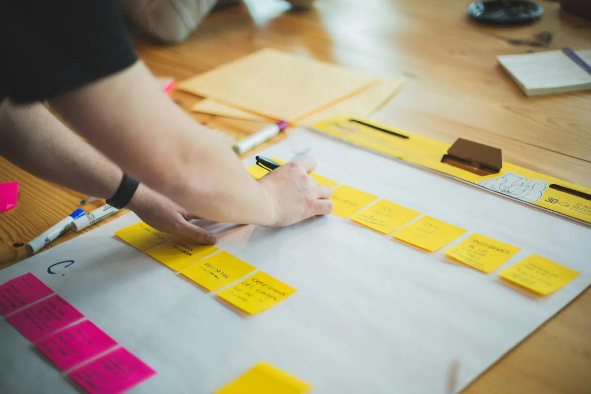 A person writes on yellow sticky notes arranged across a whiteboard on a planning table.