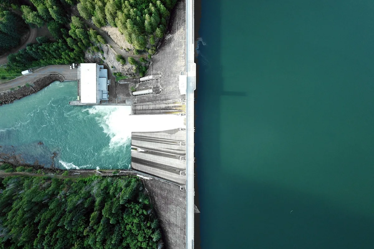 Overhead hydroelectric dam and reservoir beside woodland.